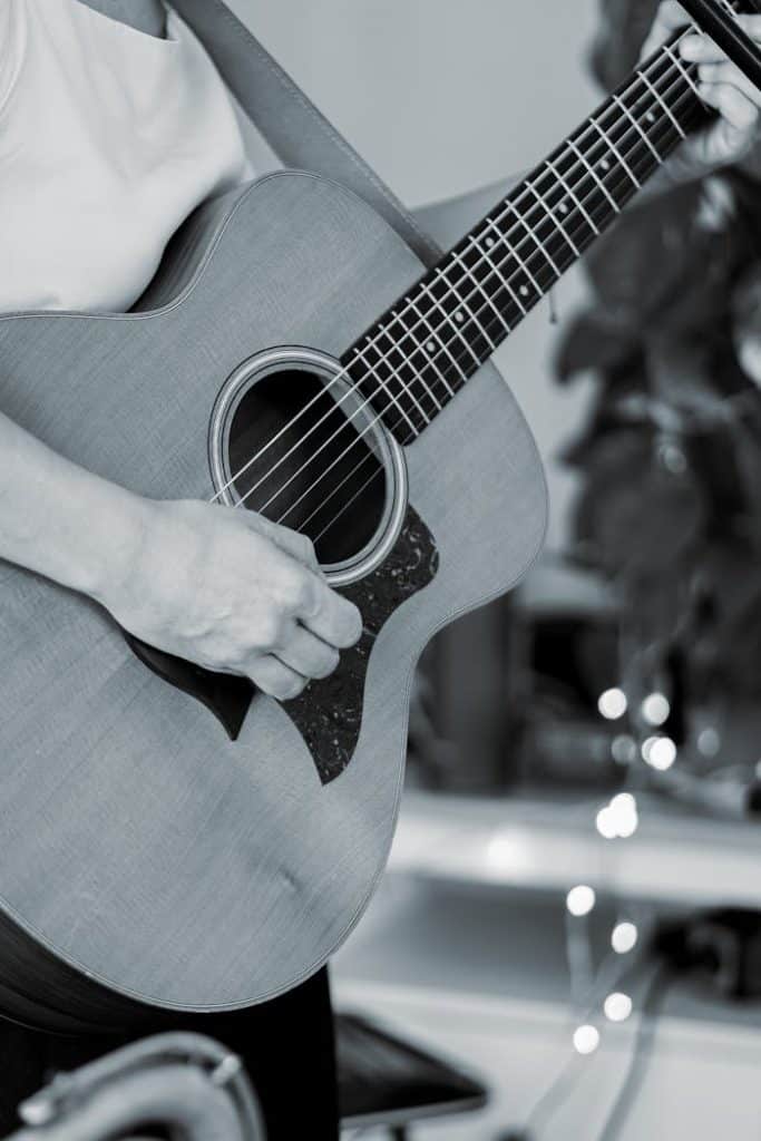 Black and white close-up of an adult playing an acoustic guitar.