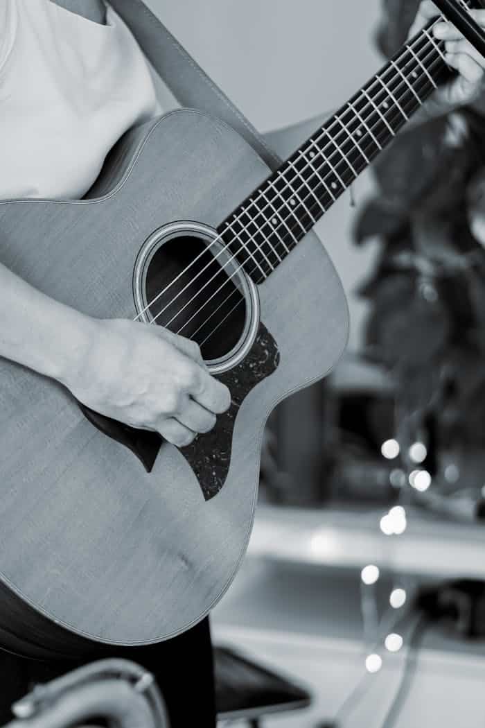 Black and white close-up of an adult playing an acoustic guitar.
